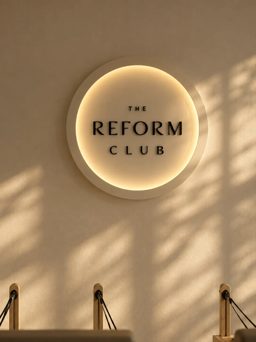 The Reform Club illuminated wall sign above a reformer in warm daylight